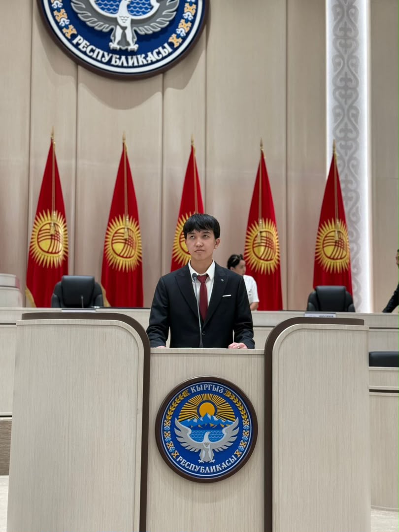 Bektur Shatmanov, founder of Youth United Alliance, standing at a podium in the Kyrgyz Republic parliament chamber